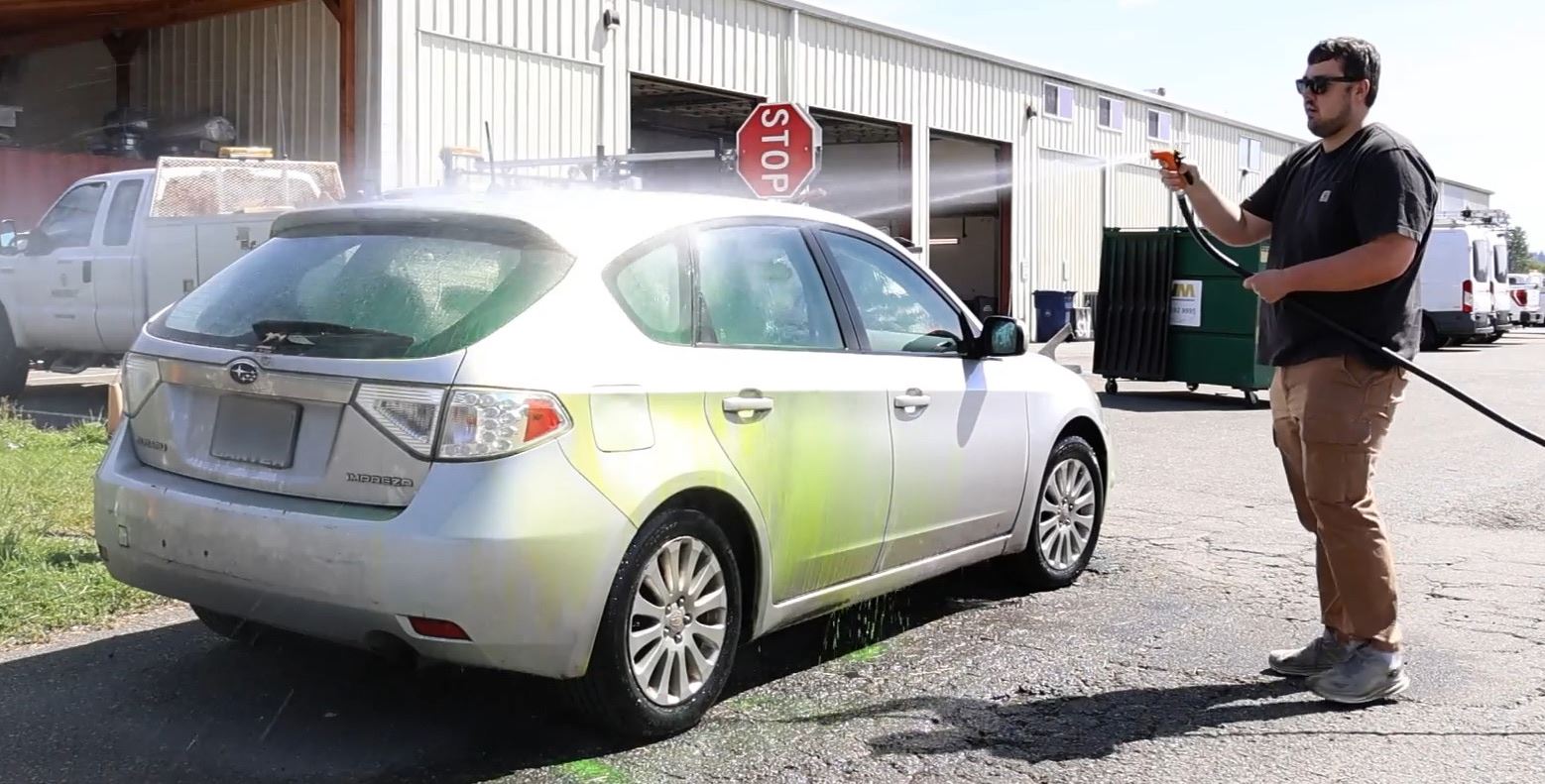 Employee using hose to wash a small, silver sedan.