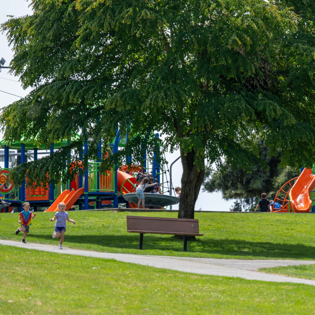 Children run down a path at Jennings Nature Park, with trees and playground equipment in background
