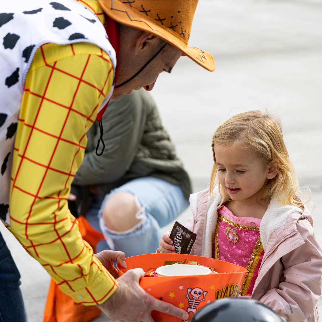 Young girl in princess costume chooses candy from a bowl held by Mayor Jon Nehring/Sheriff Woody