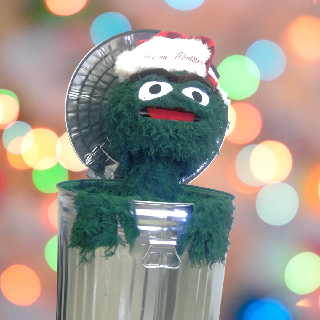 Oscar the Grouch is in a garbage can wearing a Santa hat with festive lights background